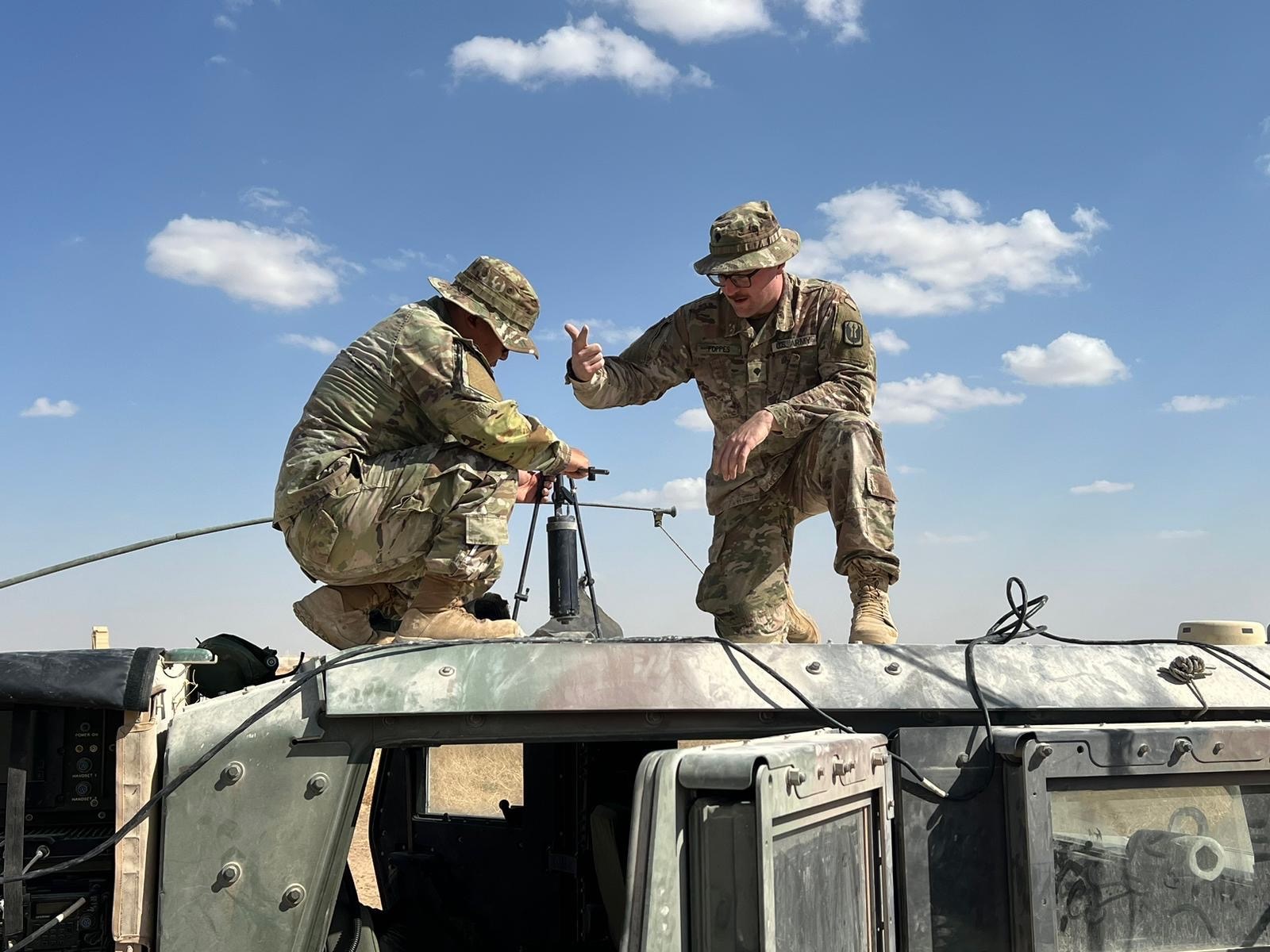 Soldiers standing setting up communications equipment on top of an army vehicle